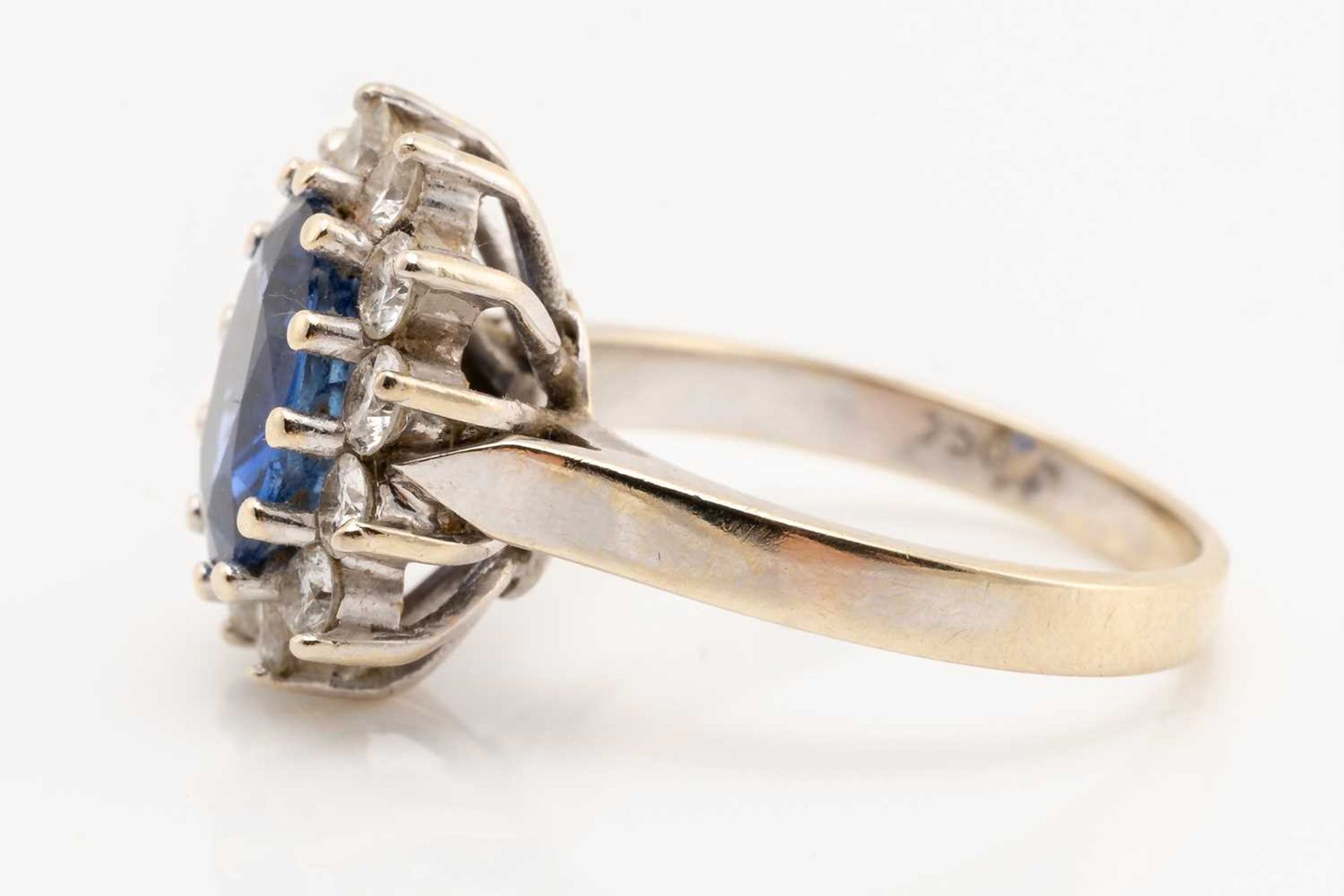 A sapphire and diamond cluster ring; the oval cut sapphire in claw mount above a border of twelve - Image 2 of 6