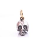 A diamond-set skull charm pendant in silver and 18ct gold, a sculpted hollow skull with eyes set