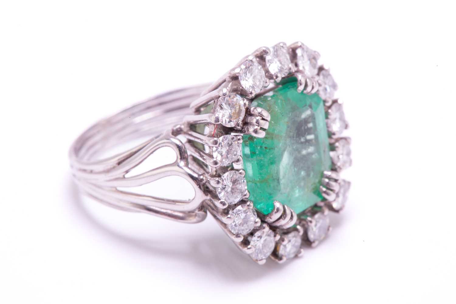 An emerald and diamond entourage ring, centred with an emerald-cut emerald of pale bright bluish- - Image 3 of 12