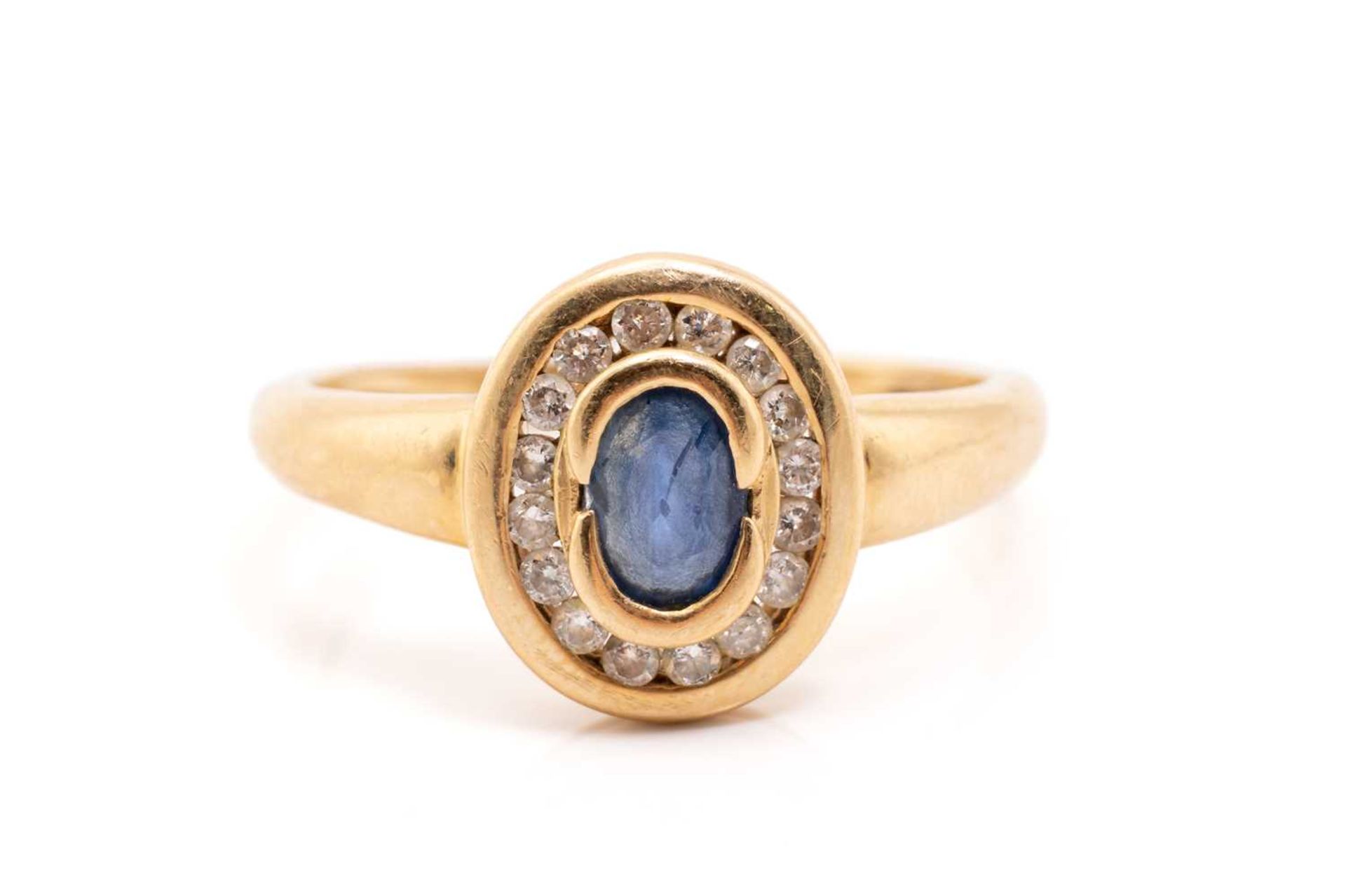 A yellow metal, sapphire and diamond halo ring, centred with an oval-cut sapphire in collet,