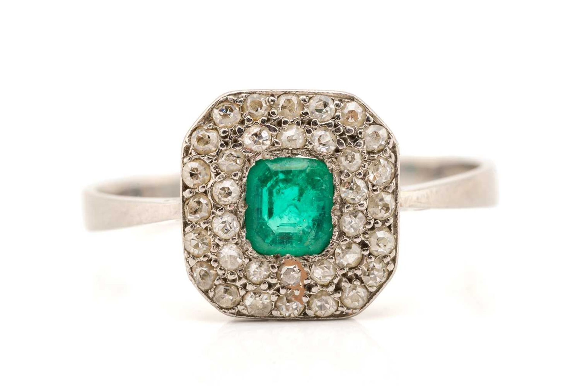 An emerald and diamond cluster ring in platinum, centred with an emerald-cut emerald of bright green