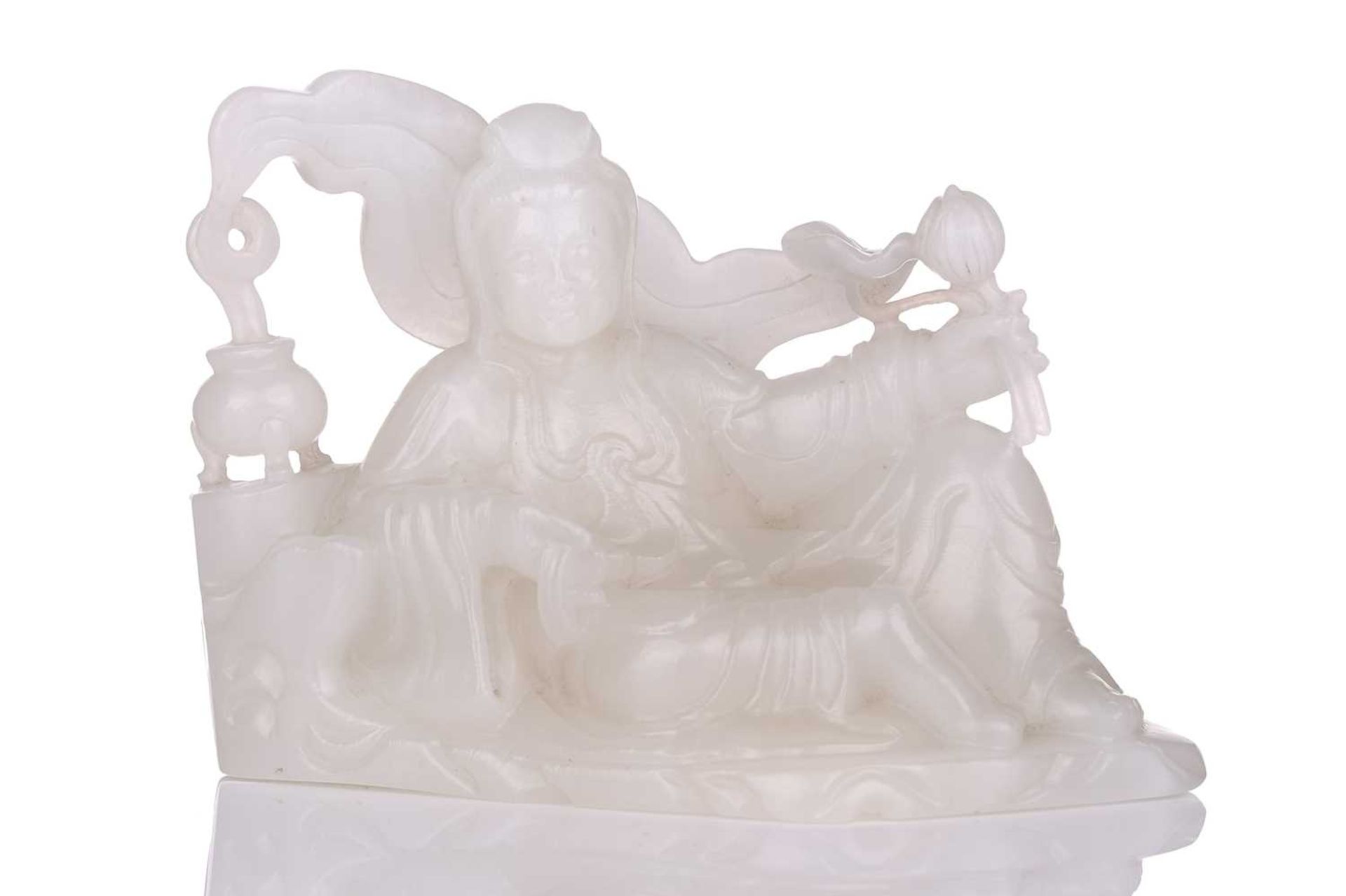 A Chinese white jade figure of Guanyin, seated in a recumbent pose with lotus flower in her left