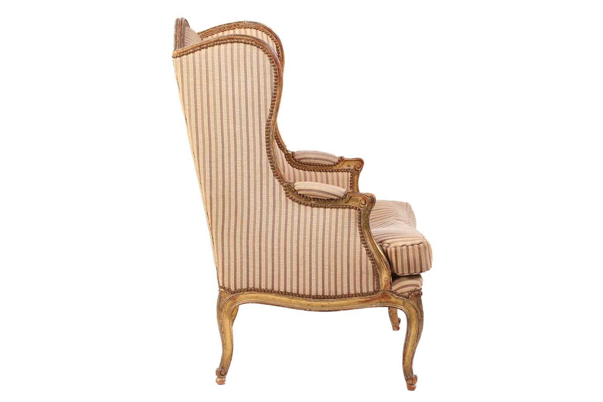 A Louis XV style bergere wing chair, 19th century, with carved wood and gilt gesso frame and striped - Image 5 of 9