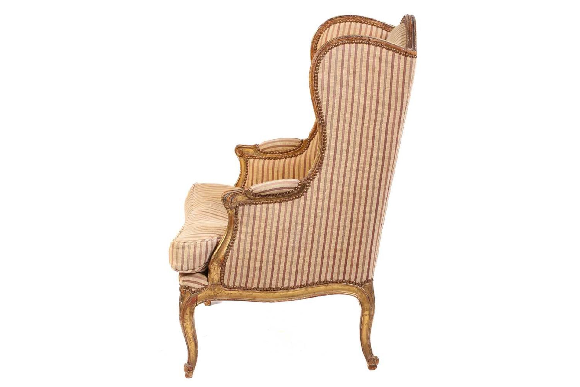 A Louis XV style bergere wing chair, 19th century, with carved wood and gilt gesso frame and striped - Image 4 of 9