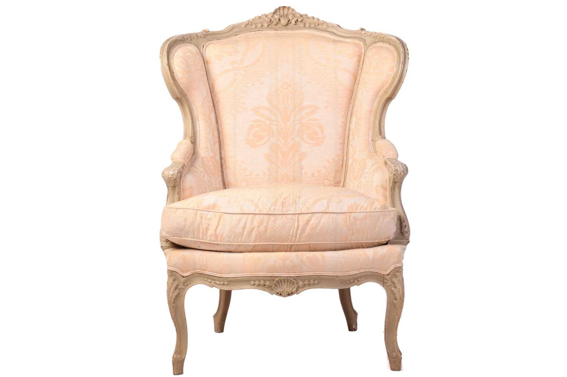A French Louis XV-style dove grey painted bergere armchair with wing back and carved shell