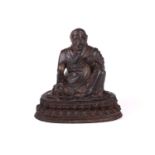 A Chinese bronze figure of a Tibetan Buddhist master, seated in robes and holding a small conch
