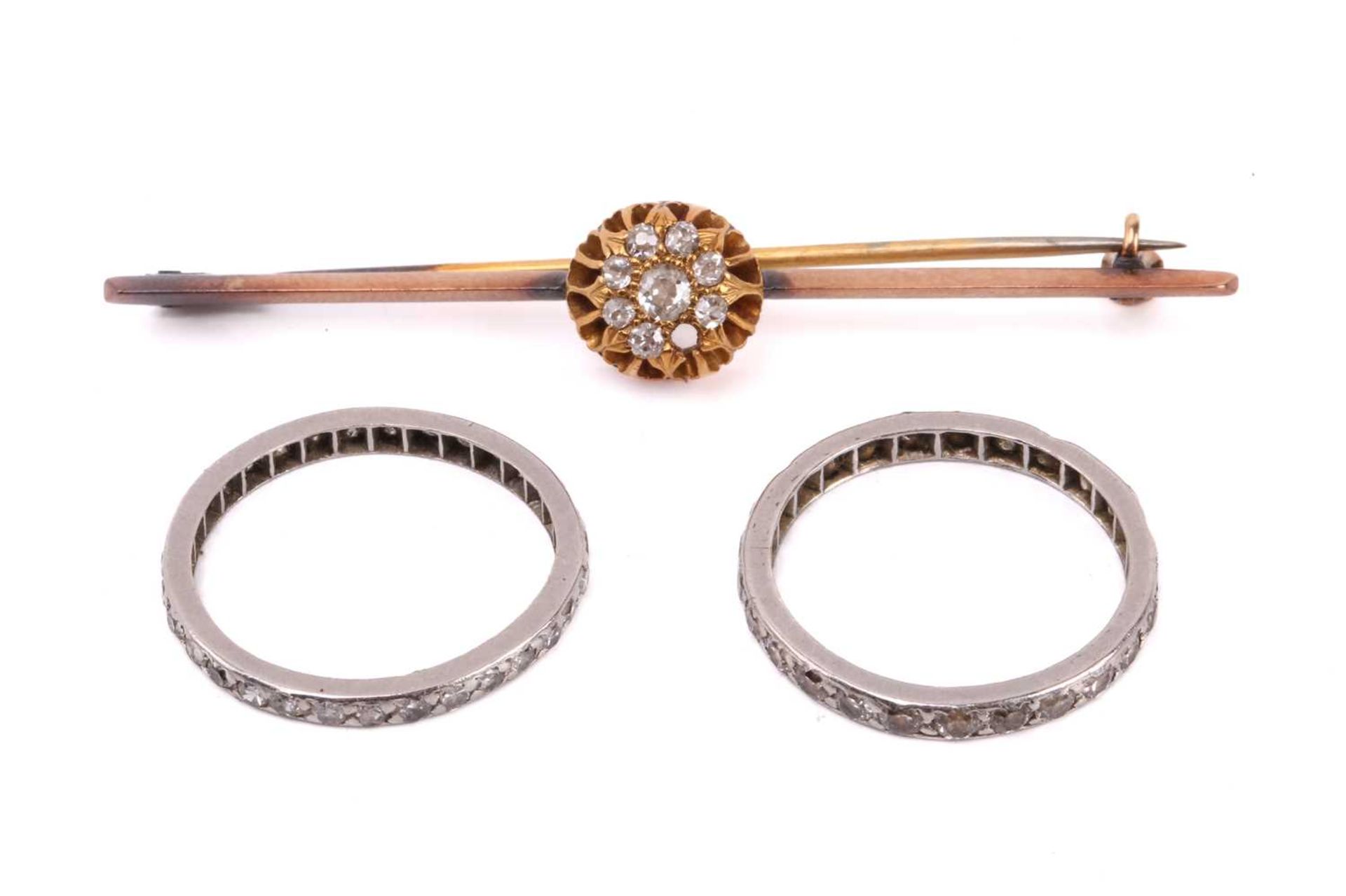 A diamond cluster bar brooch together with two diamond eternity rings. The brooch set with a cluster