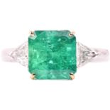 A vivid emerald and diamond three-stone ring, set with a central emerald measuring 9.2mm x 8.9mm,