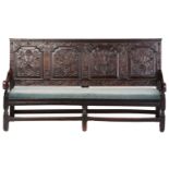 An 18th century, oak settle with carved panel back and shaped arms, the seat rails with pierced rope