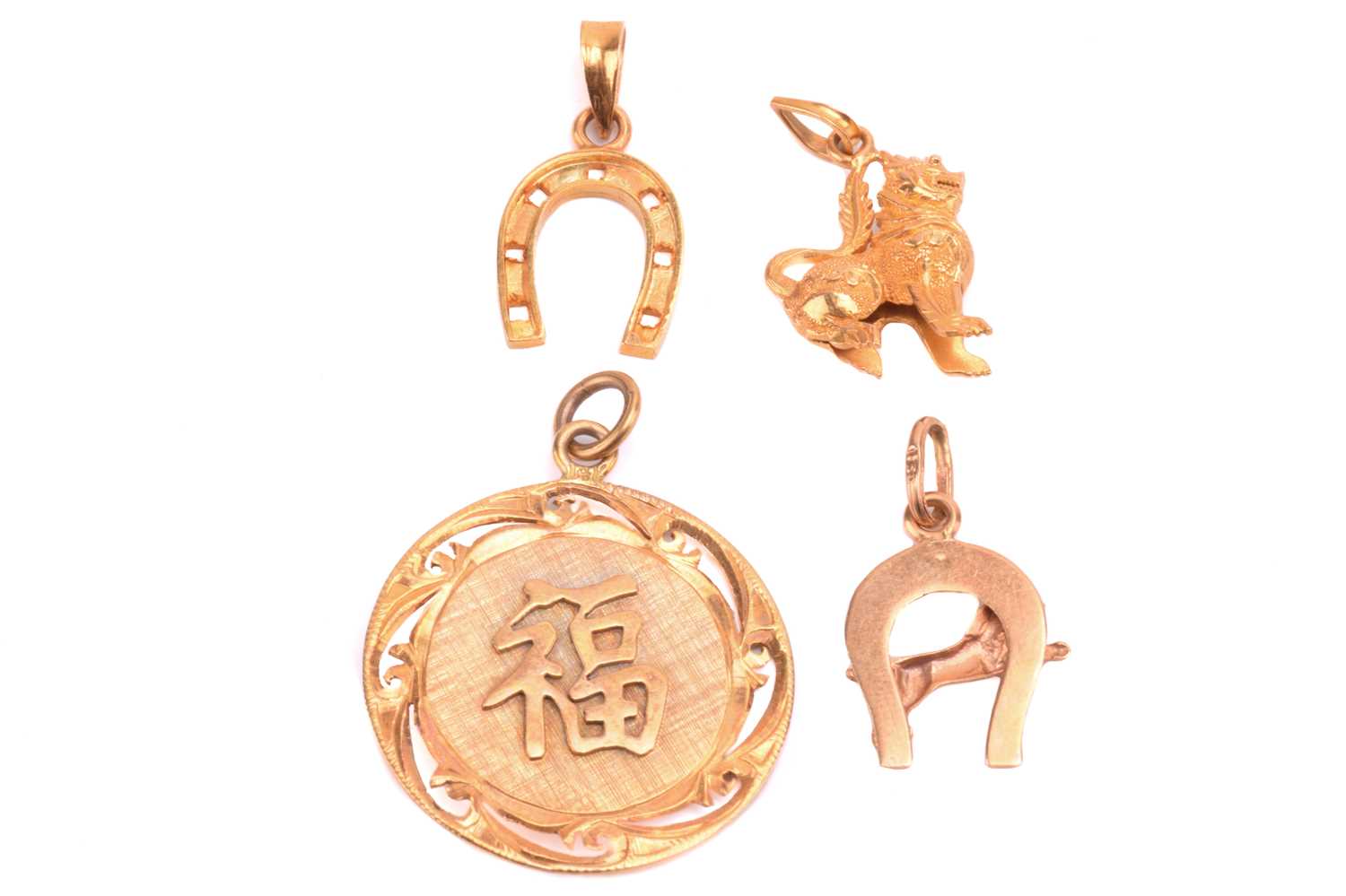 A Chinese pendant with a symbol for prosperity, a Chinese Qilin charm, and two horseshoe charms, all