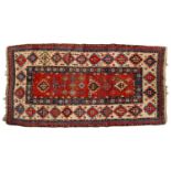 An antique Caucasian Gendje rug with soft tomato-red ground filled with cruciform lozenges, within a