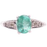An emerald and diamond ring; the oval cut emerald, claw mounted above-carved shoulders with two