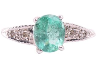 An emerald and diamond ring; the oval cut emerald, claw mounted above-carved shoulders with two