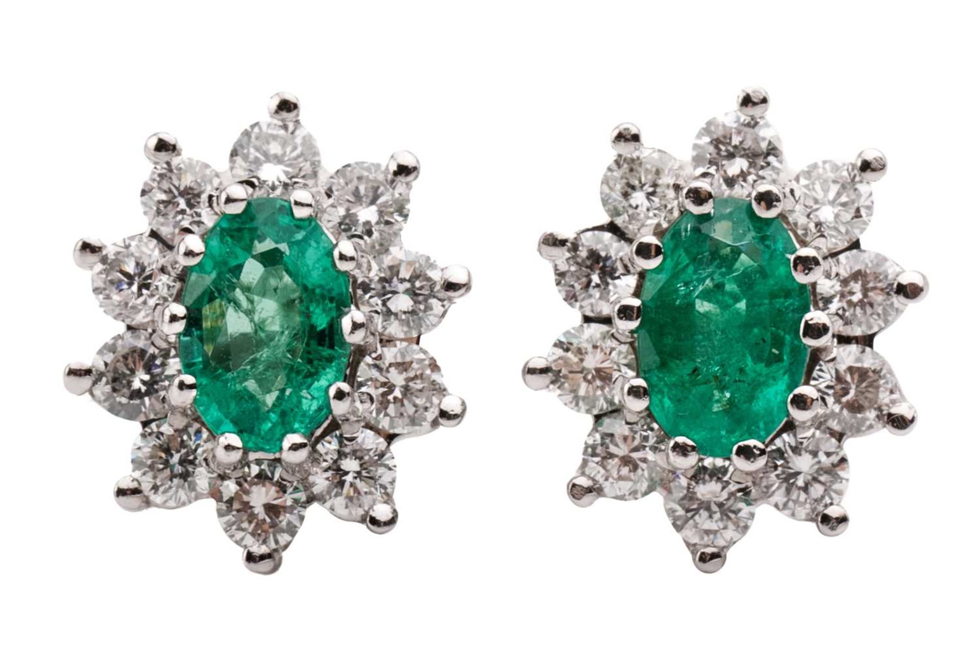 A pair of 18 carat white gold, emerald and diamond earrings; the oval cut emeralds in claw mounts