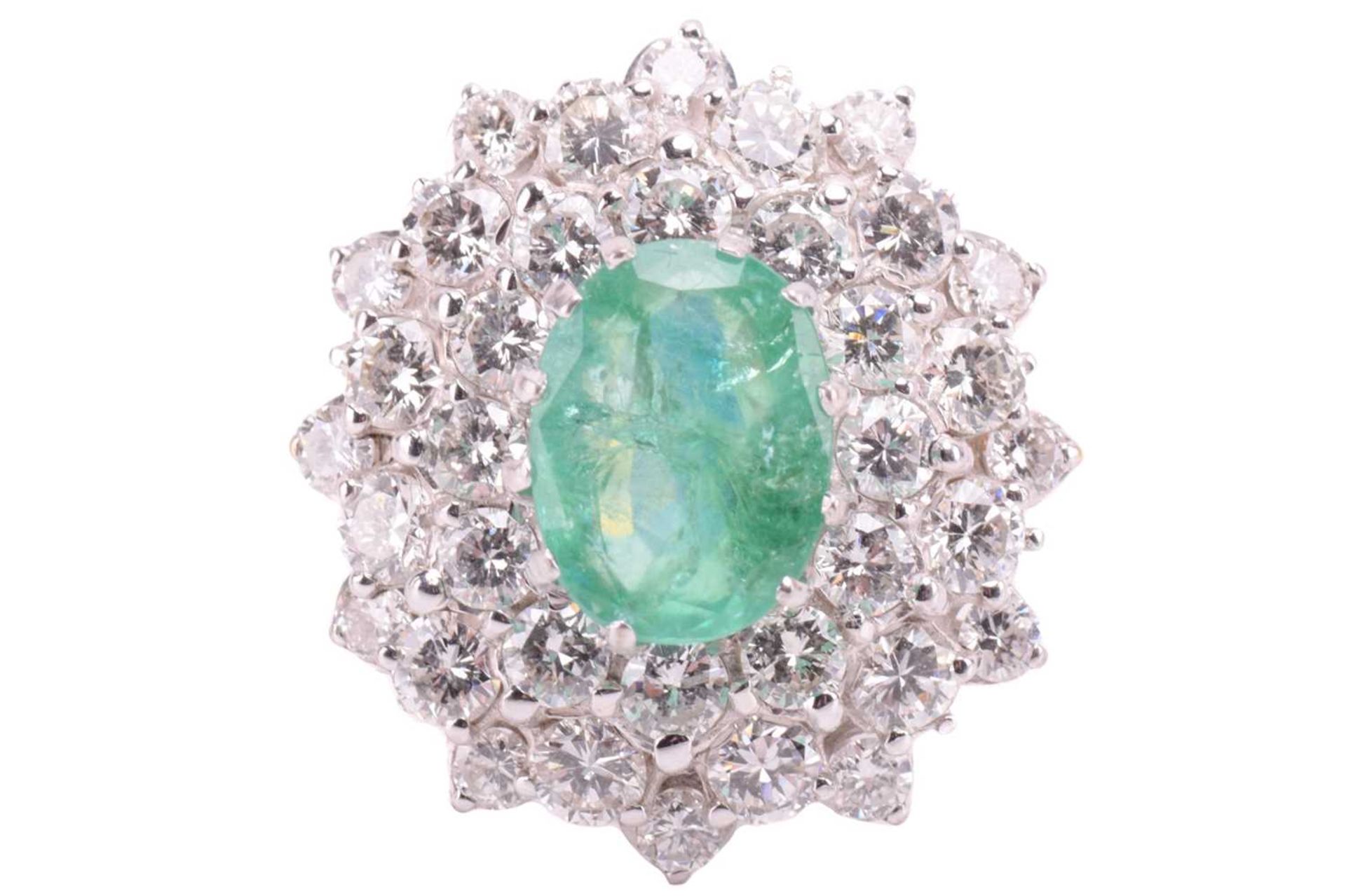 An emerald and diamond cluster ring, the fracture-filled emerald centrally set within a cluster of