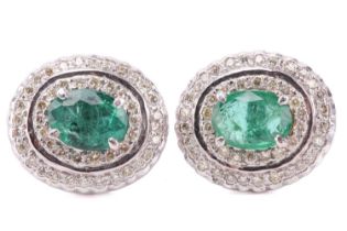 A pair of emerald and diamond cluster earrings, each featuring an oval-cut emerald of bright green