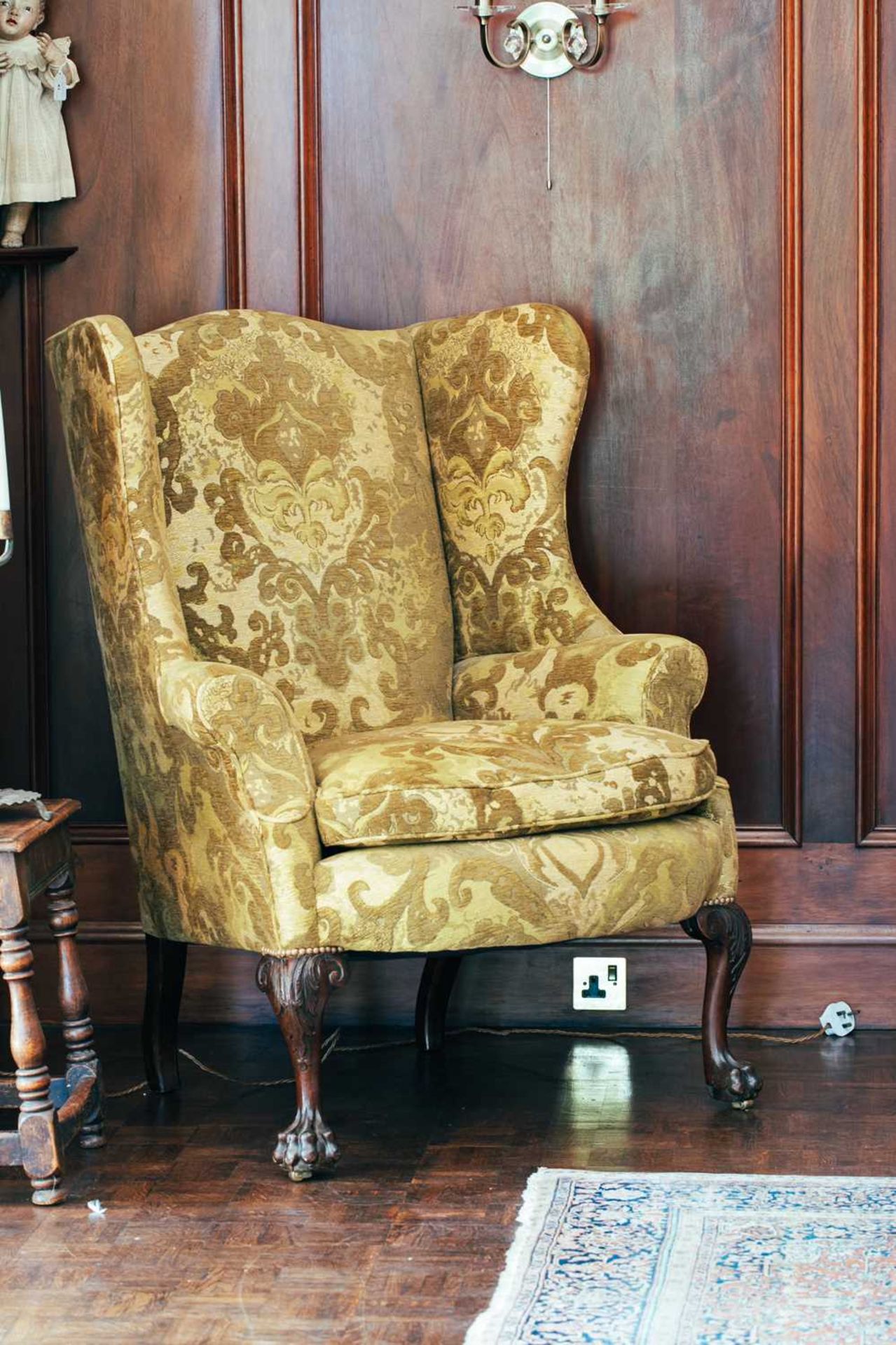 A large George III style upholstered mahogany wing armchair, on scroll-carved cabriole legs, lion