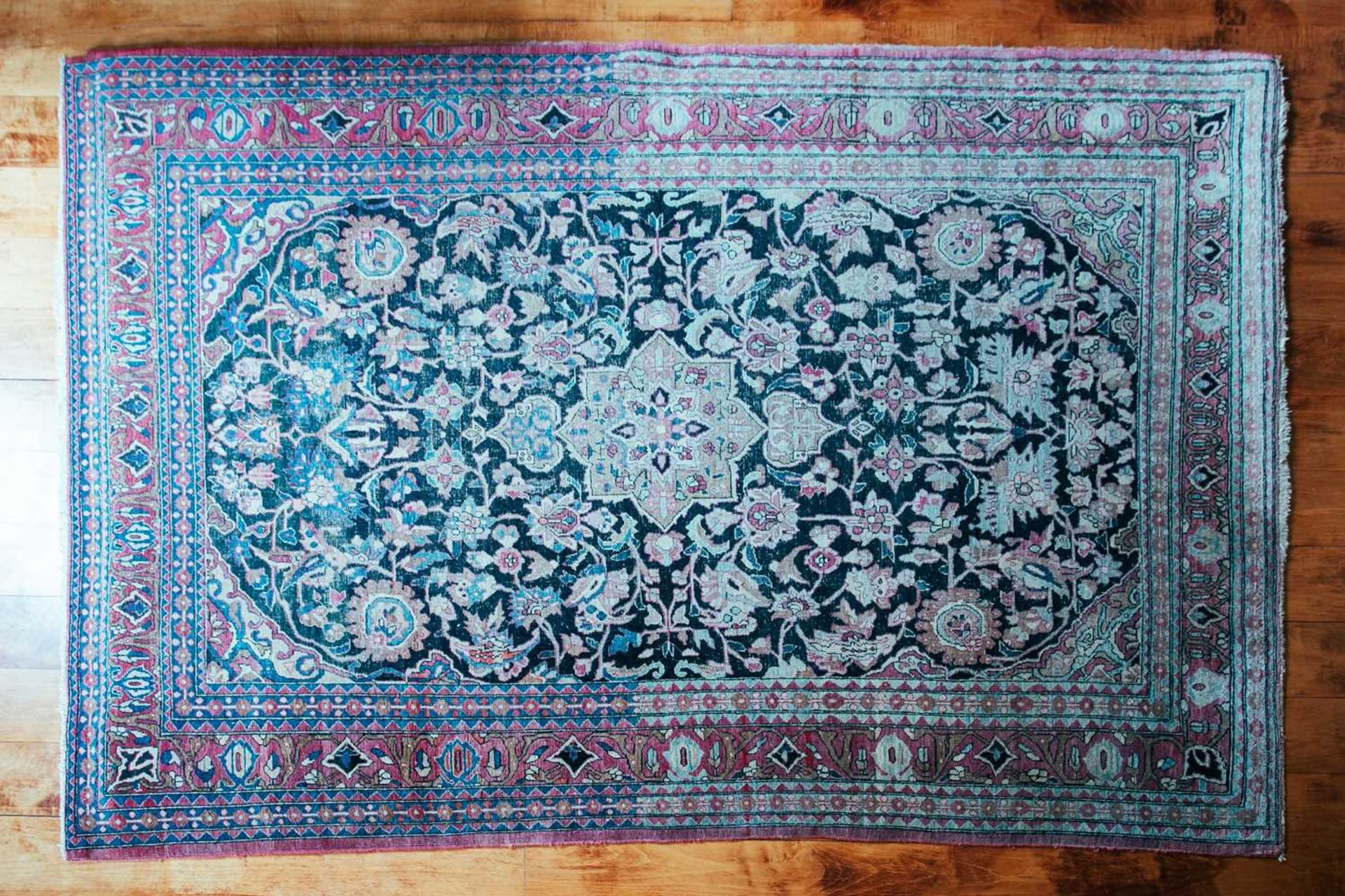 An antique black/blue ground Kerman carpet, with a central star and corners with multiple vines