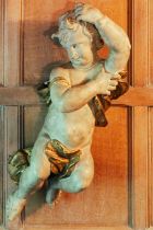 An 18th century Northern European painted softwood cherub, with curly hair swathed in a billowing
