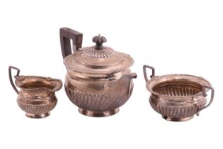 A late Victorian silver three-piece tea service, the teapot with wooden knop and handle, half-reeded