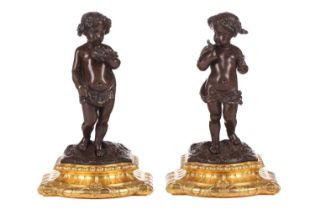 A pair of bronze figures of standing putti holding a dove and a nest, on ormolu cabochon design