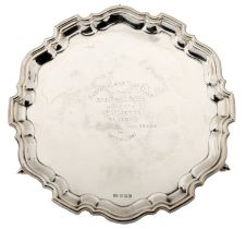 A silver presentation salver, with piecrust border and central inscription, on scroll feet,...