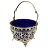 A PIERCED SILVER SUGAR BOWL, with blue glass liner, pierced floral panel sides and swing handle,