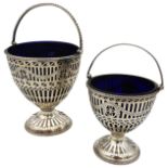 TWO GEORGE III SILVER SUGAR BASKETS, with blue glass liners, hand cut pierced sides with foliate