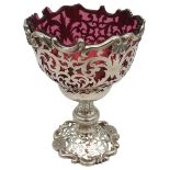 AN ORNATE PIERCED SILVER VASE, chalice form, with a cranberry glass liner, the ornate scrolling
