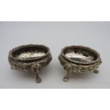 A PAIR OF SILVER PLATED SALTS, gadrooned rims with scroll foliate repousse decoration