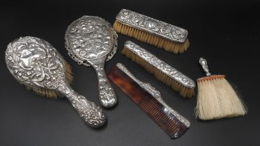 A SILVER BACKED MIRROR, FOUR VARIOUS SILVER MOUNTED BRUSHES AND COMB, all with ornate floral and