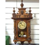 Wooden cased antique 8 day wall clock with RA printed pendulum, 6 wooden finials, turned pillars and