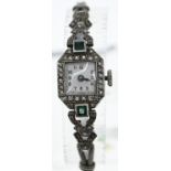 Platinum cased Art Deco watch set with diamonds and green stones on a white metal strap (testing pos