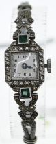 Platinum cased Art Deco watch set with diamonds and green stones on a white metal strap (testing pos