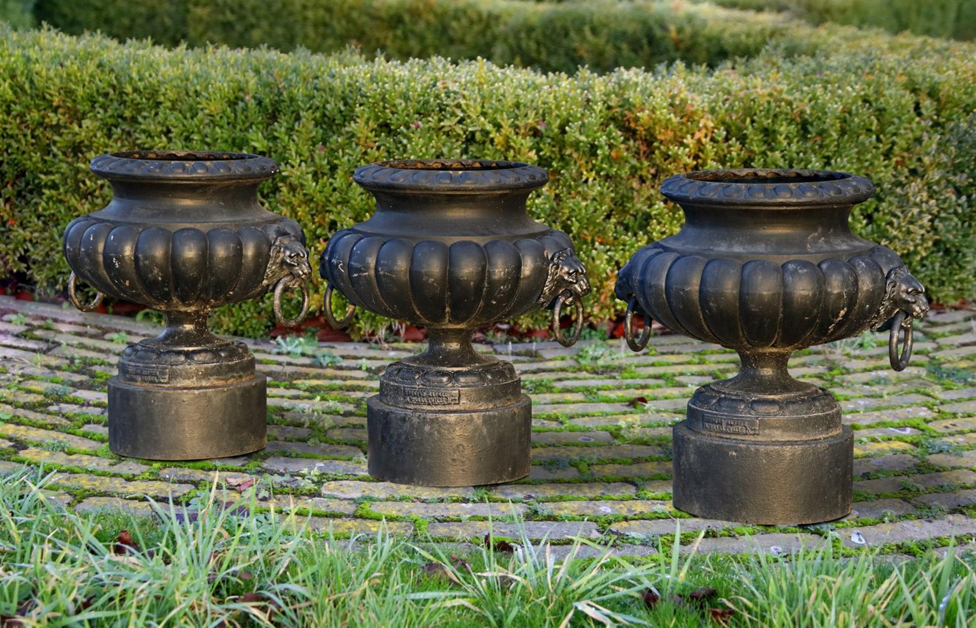 ‡ A SET OF THREE BLACK PAINTED CAST IRON VASES