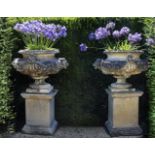 Ω A PAIR OF COMPOSITION STONE GARDEN URNS ON PLINTHS