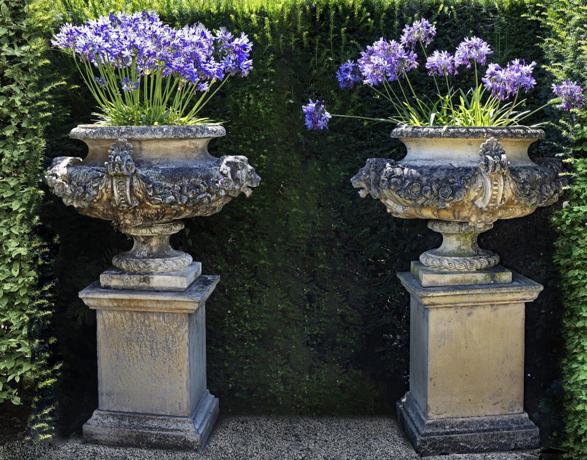 Ω A PAIR OF COMPOSITION STONE GARDEN URNS ON PLINTHS