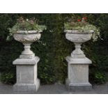 Ω A PAIR OF COMPOSITION STONE PEDESTAL URNS ON PLINTHS