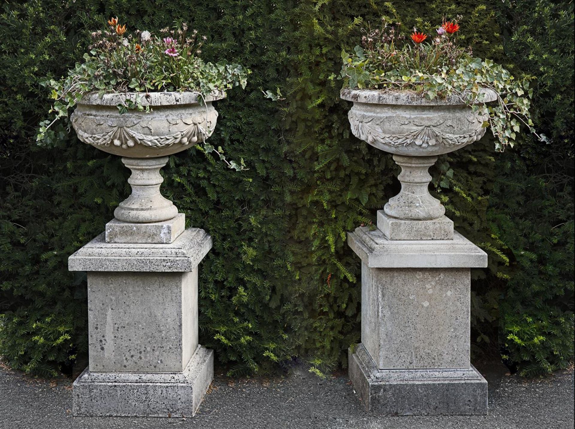 Ω A PAIR OF COMPOSITION STONE PEDESTAL URNS ON PLINTHS