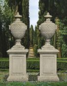 Ω A PAIR OF CARVED LIMESTONE URNS ON PEDESTALS