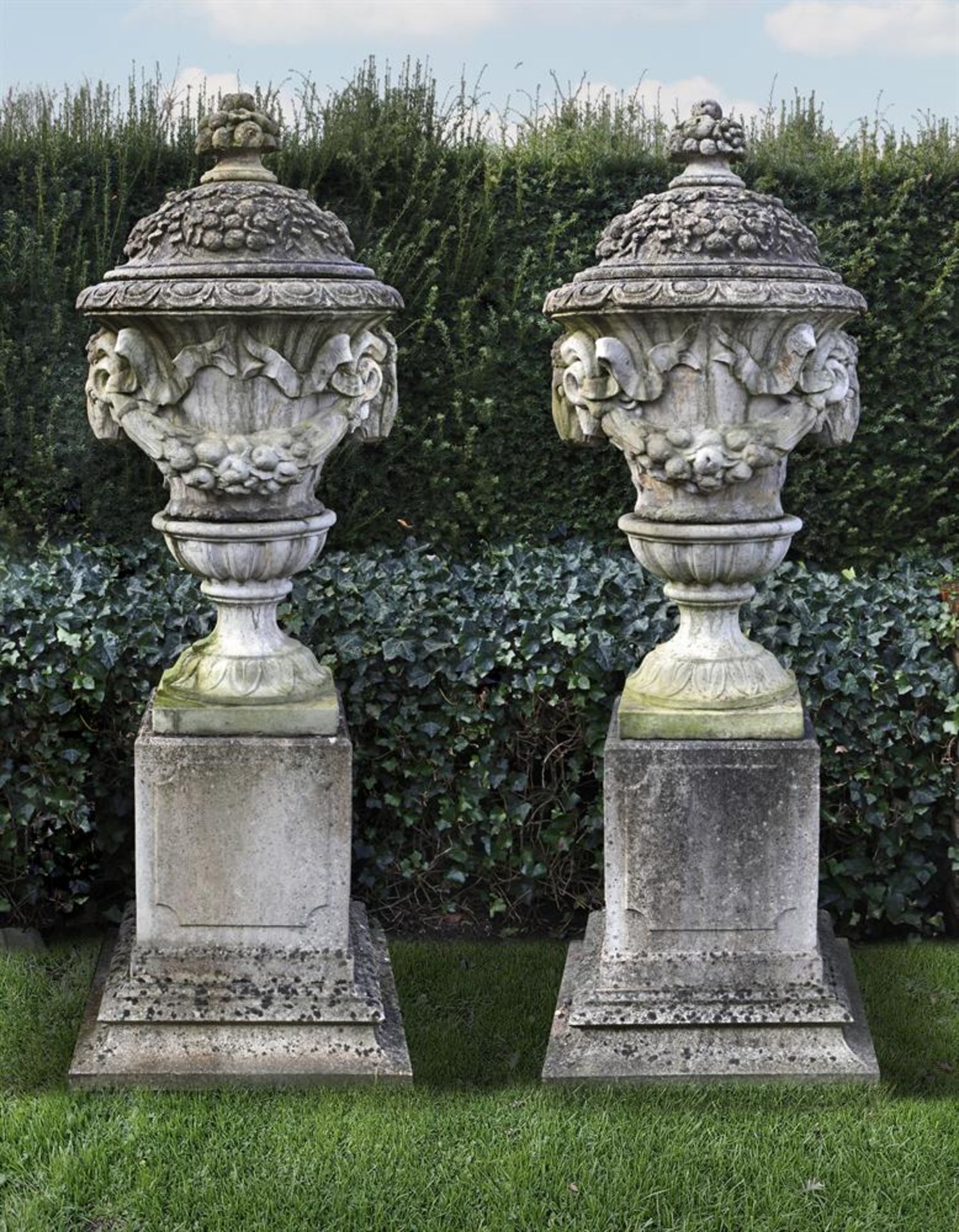 Ω A PAIR OF COMPOSITION STONE GARDEN URNS ON PLINTHS