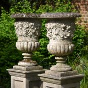 A PAIR OF COMPOSITION STONE VINE PATTERN URNS ON STANDS IN THE ITALIAN MANNER, MODERN