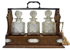 Edwardian oak three bottle tantalus with plated mounts