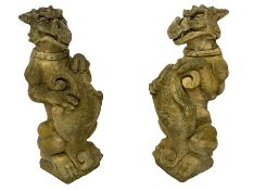 Pair of composite stone garden ornaments in the form of griffins or gargoyles holding cartouche shie