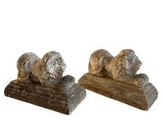 Pair of cast stone garden figures in the form of recumbent lions holding balls between their paws