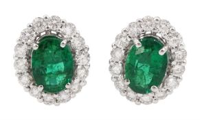 Pair of white gold oval cut emerald and round brilliant cut diamond cluster stud earrings