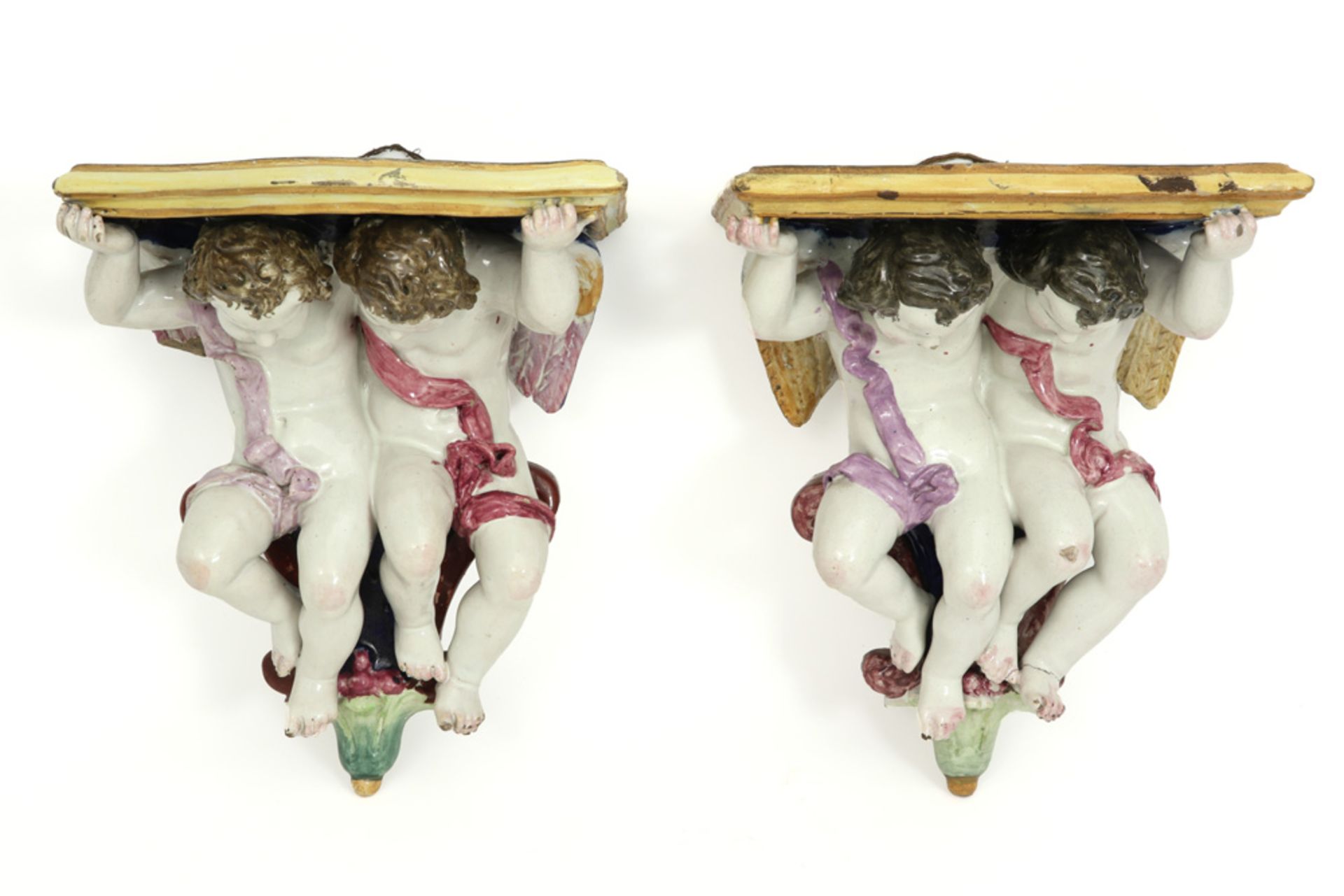 pair of Italian wall hanging consoles, each with two cupids, in polychromed ceramic 