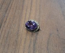 A Victorian yellow metal mounted halo brooch set with a central oval amethyst, surrounded by seed