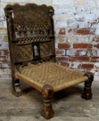 A 19th century Indian Pida Rajasthani low chair, the chip carved geometric panelled wooden back rest