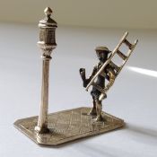 A Dutch style silver miniature of a lamplighter and lamp on a rectangular base decorated with paving